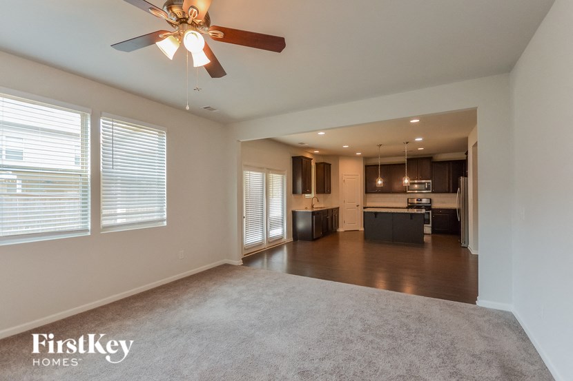 an empty living room with a ceiling fan and a kitchen