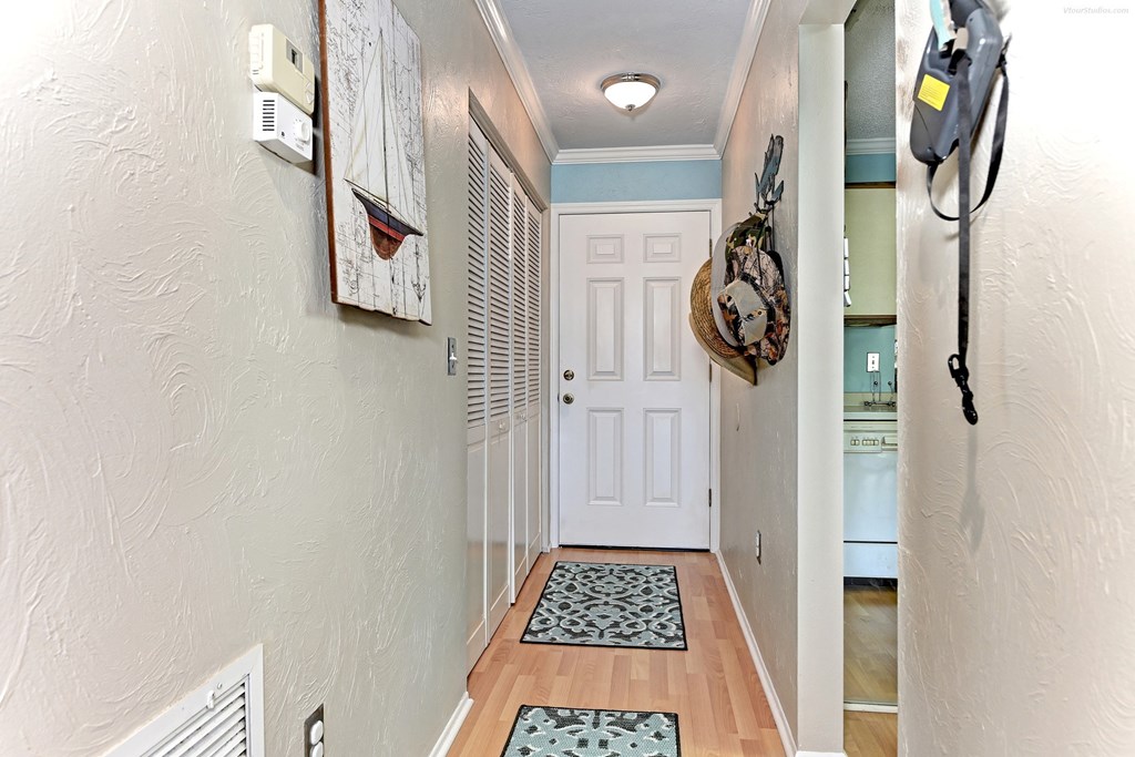 the hallway to the front door of a house with a backpack hanging on the wall