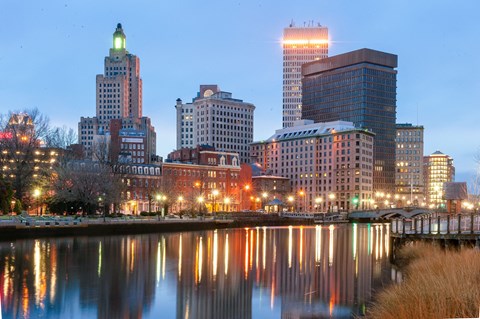 A cityscape at dusk with buildings reflecting in the water.