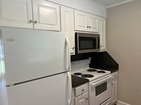 A white refrigerator is in a kitchen with white cabinets and a black countertop.