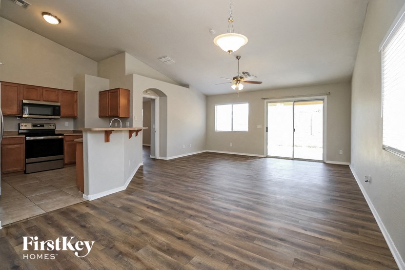an empty living room with a kitchen and a ceiling fan