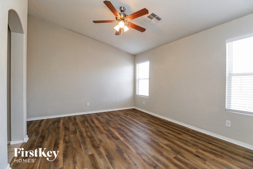 the spacious living room with hardwood flooring and a ceiling fan