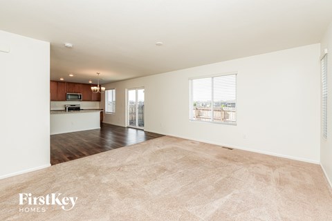 A spacious living room with a carpeted floor and a view of the kitchen through the window.