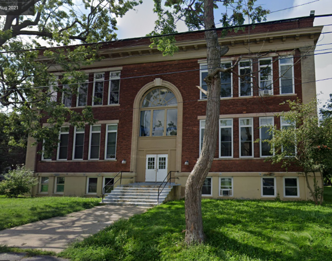 the front of a red brick school building with a tree in front