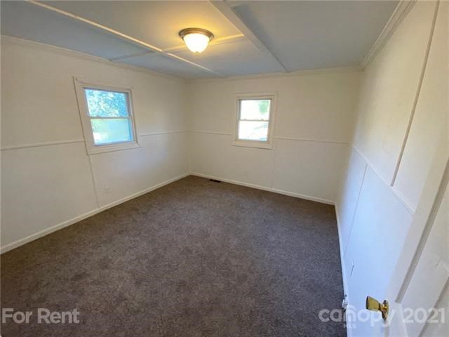 a small room with a carpet and two windows