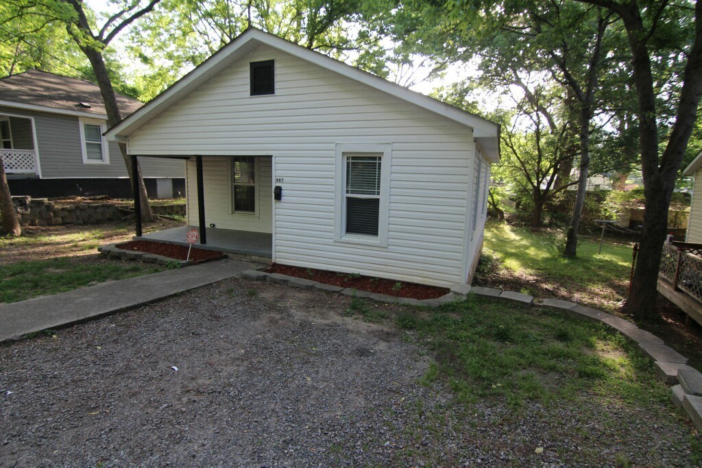 the front of the house has a gravel driveway and plenty of trees