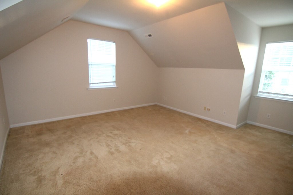 an empty bedroom with carpet and two windows