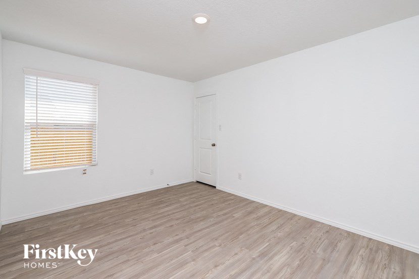 a bedroom with white walls and wood flooring and a window