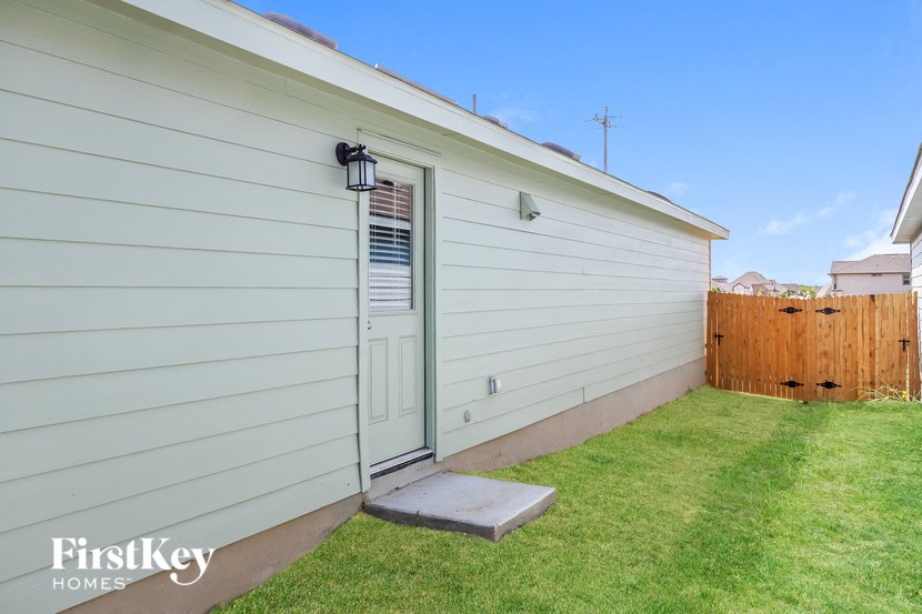 the backyard of a white house with a blue door and a green lawn