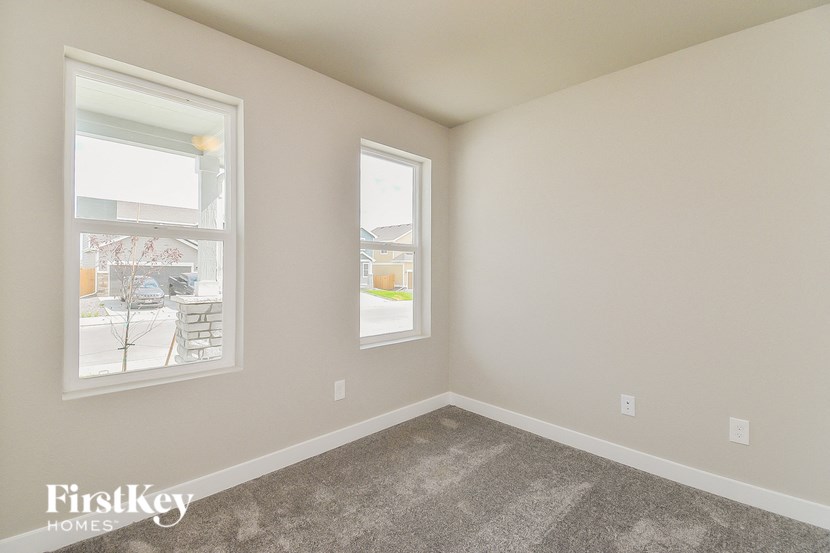 the living room of an apartment with carpet and two windows