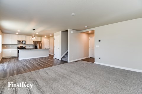 A spacious living room with a kitchen in the background and a carpet on the floor.