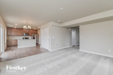 A spacious living room with a kitchen in the background and a carpet on the floor.