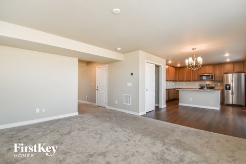 A spacious, empty living room with a kitchen in the background.