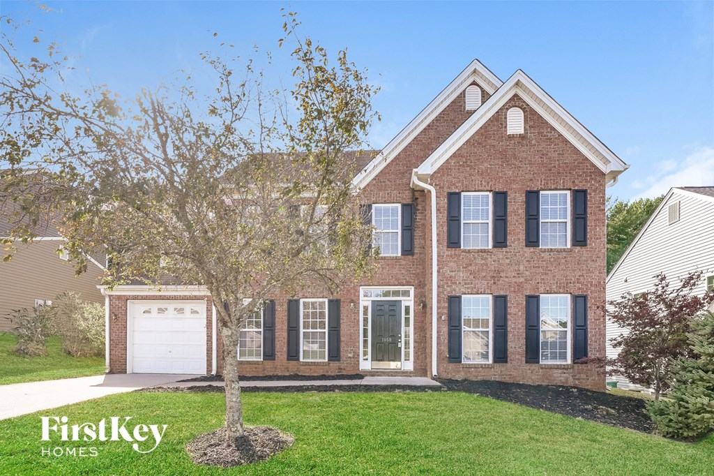 a brick house with a white garage and a tree in the yard