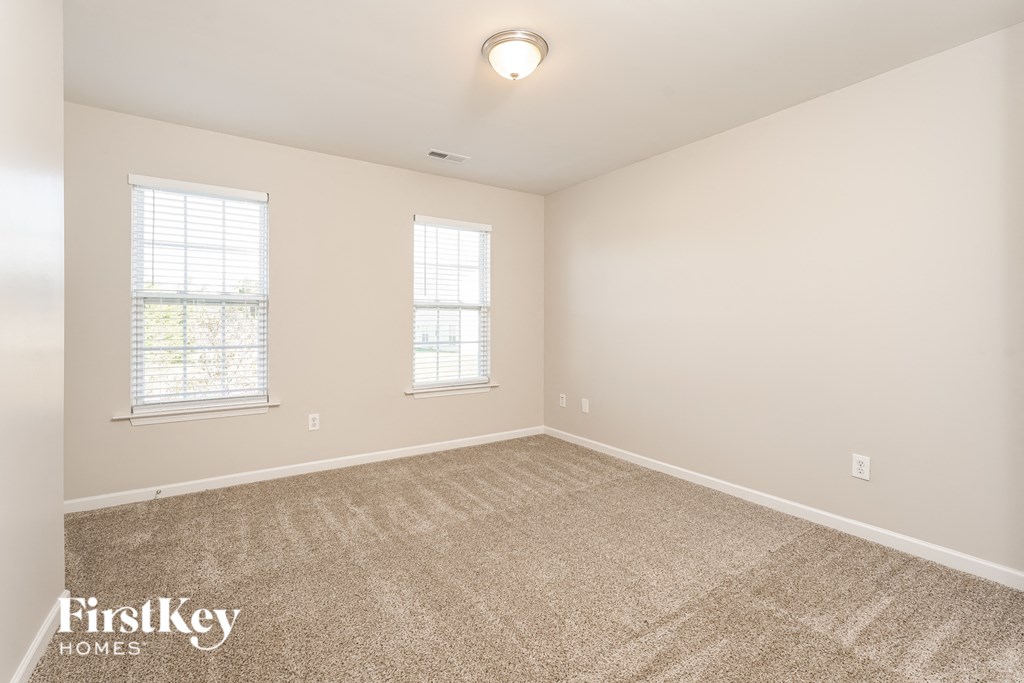a spacious living room with carpet and two windows