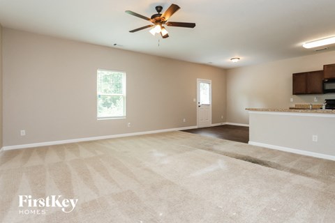 an empty living room with a ceiling fan and a kitchen