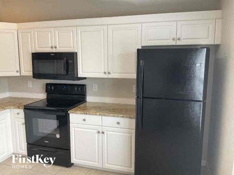 A black refrigerator sits in a kitchen with white cabinets.