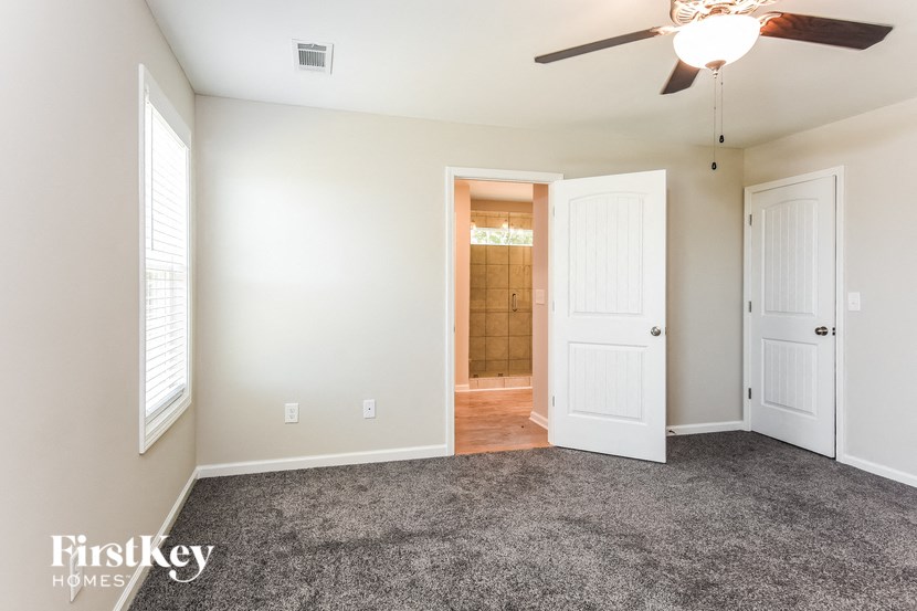 an empty living room with a ceiling fan and a door to a bathroom
