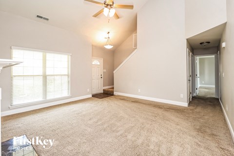 A spacious room with a carpeted floor, a ceiling fan, and a staircase leading to another level.