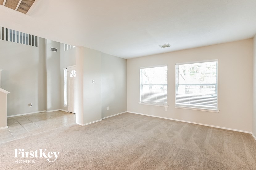 an empty living room with three windows and beige carpet