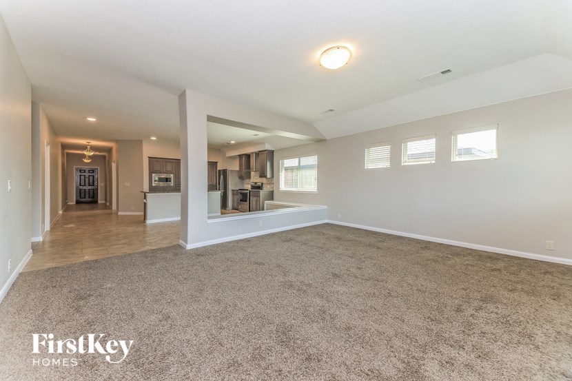 an empty living room with a kitchen in the background