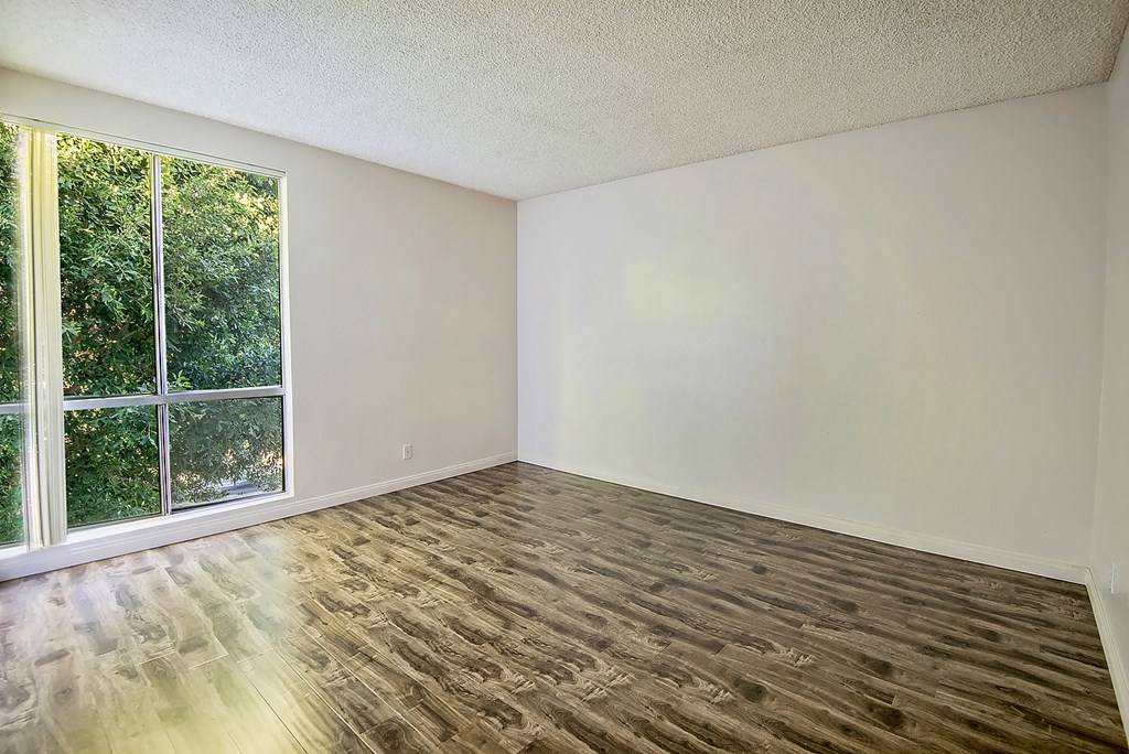 an empty living room with a large window and wooden floors