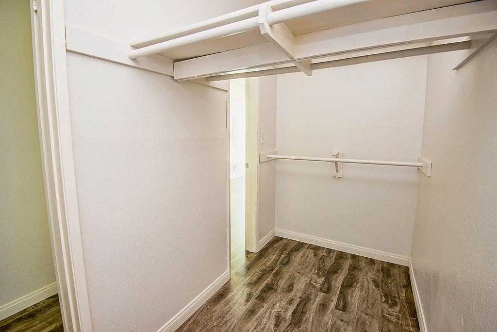 a walk in closet with a wood floor and white walls
