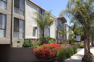 an apartment building with palm trees and flowers in front of it