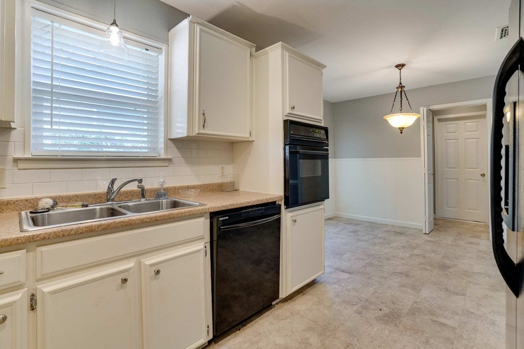 a kitchen with white cabinets and a black dishwasher and sink