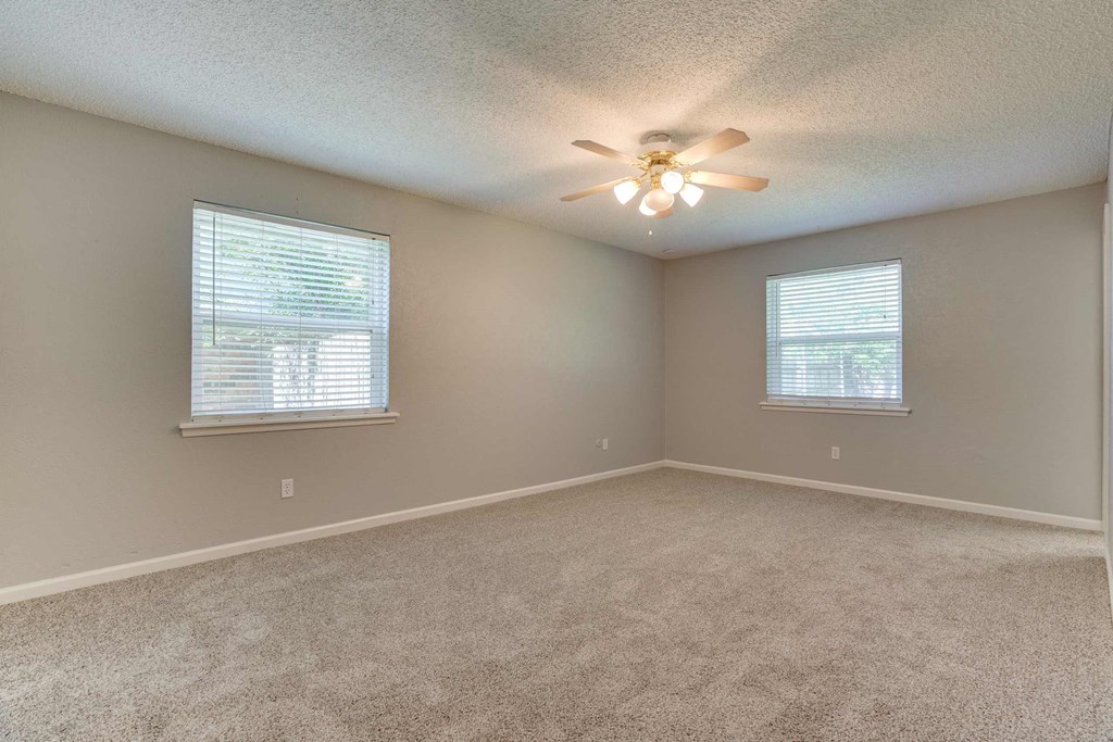 an empty living room with a ceiling fan and two windows