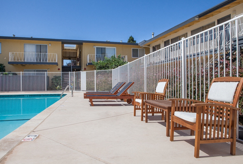 a patio with chairs and a pool in front of a building