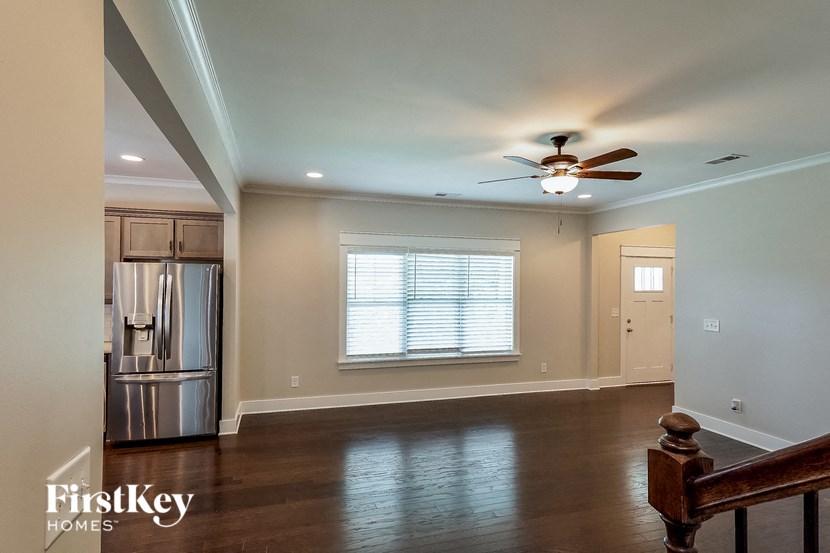 a empty living room with a ceiling fan and a kitchen