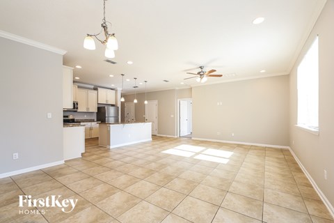 A spacious living room with a kitchen in the background and a ceiling fan above.