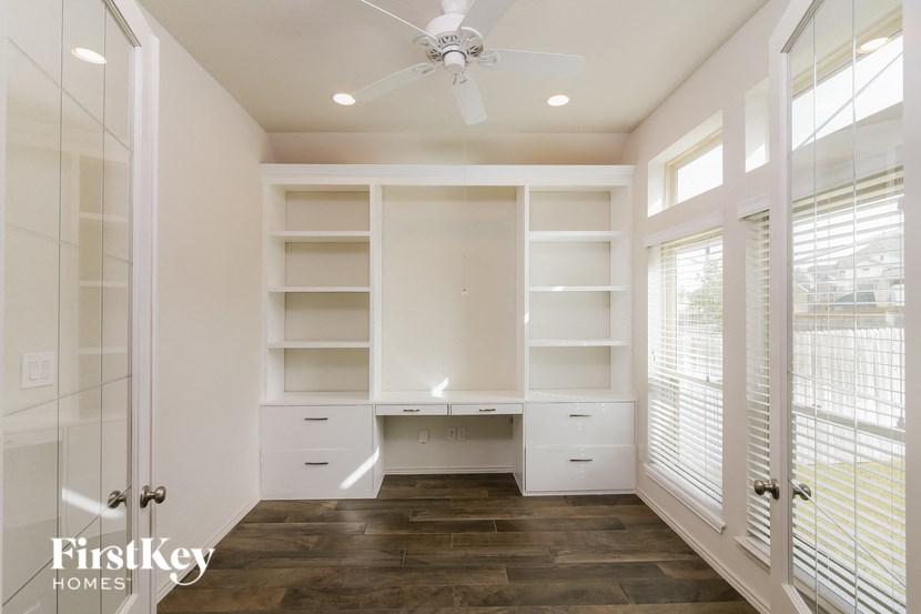 a walk in closet with white shelves and a ceiling fan