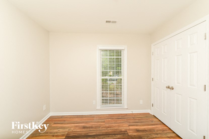 a bedroom with white walls and a window and wood floors