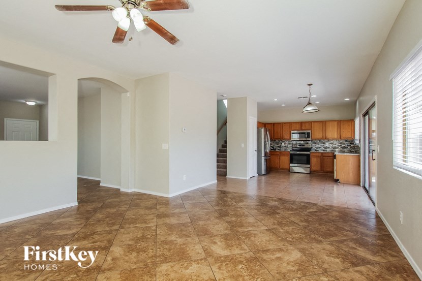 A spacious living room with a fan and a kitchen in the background.