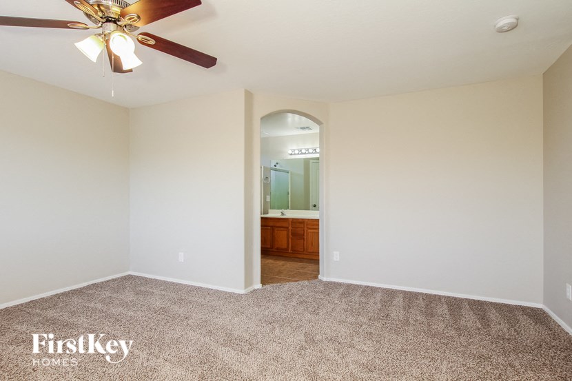 A carpeted room with a ceiling fan and a doorway leading to another room.