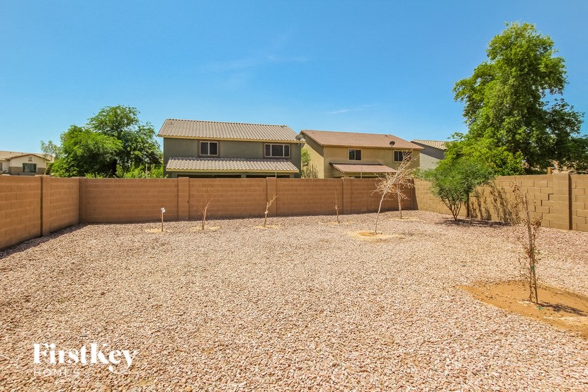 A gravel backyard with a fence and a small tree.