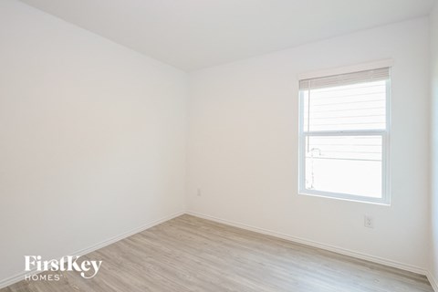 a bedroom with white walls and a window and wood floors