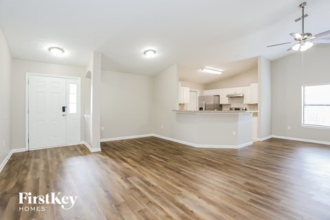 an empty living room with wood flooring and a kitchen