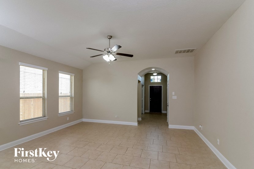 an empty living room with a ceiling fan and a hallway