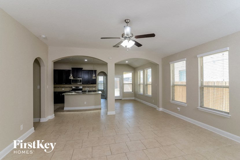 an empty living room with a ceiling fan and a kitchen