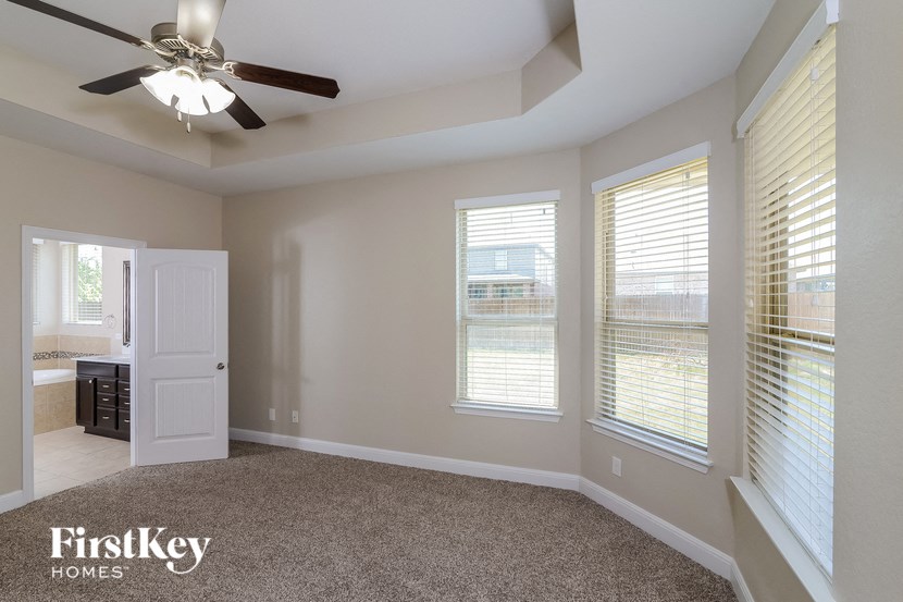 an empty living room with a ceiling fan and three windows
