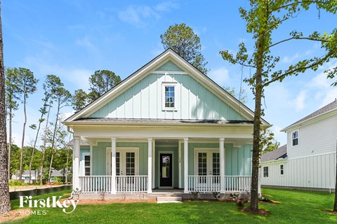 A small house with a porch and a tree in front of it.