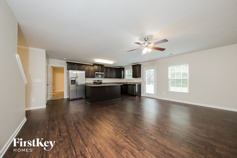 an empty living room and kitchen with wood flooring and a ceiling fan