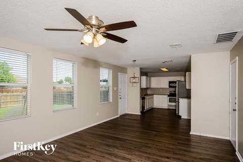 A spacious living room with a ceiling fan and wooden floors.