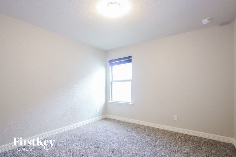 A room with a carpeted floor, a window, and a light on the ceiling.