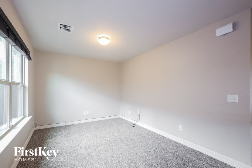 A spacious room with a carpeted floor and a window on the left side.