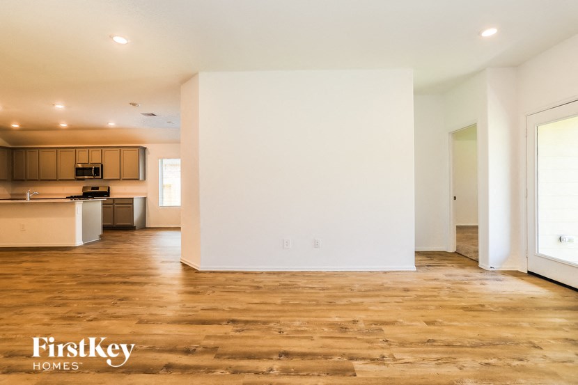 A spacious room with wooden flooring and a kitchen area in the background.