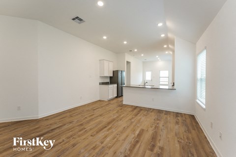 A spacious room with wooden flooring and white walls, with a kitchenette in the corner.
